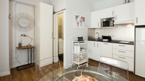 Una cucina moderna con mobili bianchi, un forno a microonde, un frigorifero e un tavolo da pranzo in vetro con pasticcini.