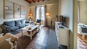 Un salon avec un canapé gris, une table basse à motifs et un bureau blanc avec un ordinateur.