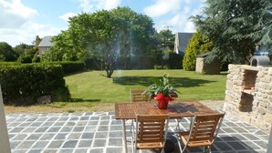 An outdoor patio with a stone floor, a wooden table, and chairs. There is a potted plant on the table. - Longere with seaside view (Cancale)