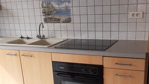 A kitchen with wooden cabinets, a black oven, a tiled backsplash with a maritime mural, and a sink with a faucet. - Longere with seaside view (Cancale)