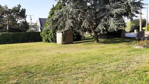 A grassy yard with a stone structure, a large tree, and a hedge. - Longere with seaside view (Cancale)