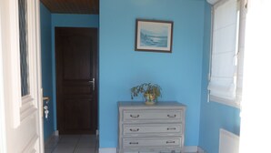 A hallway with a blue wall, a wooden door, a white dresser with drawers, and a framed picture on the wall. - Longere with seaside view (Cancale)