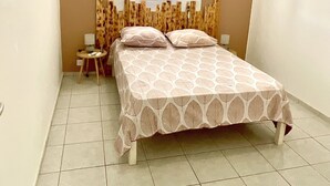 A bedroom with a bed, a small table, a window with a curtain, and an air conditioning unit on the wall.