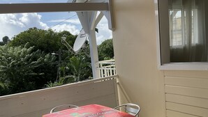A covered outdoor patio with a table and chairs, a satellite dish, and a view of greenery.