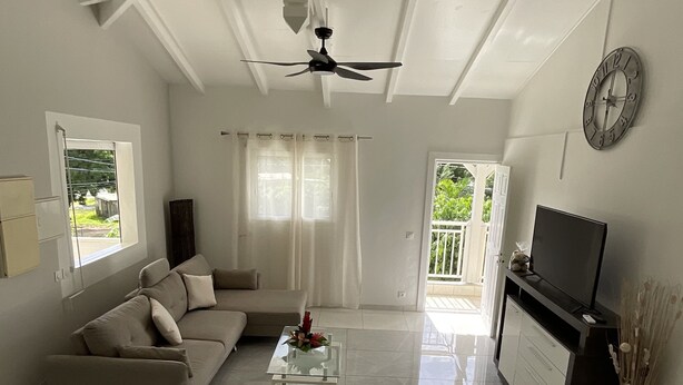 A spacious living room with a sofa, a coffee table, a TV, and a ceiling fan.