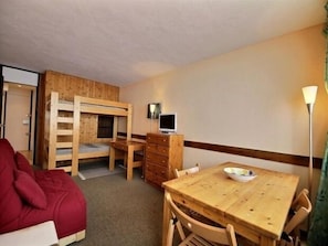 A room with a bunk bed, a desk with a computer, a dining table with chairs, and a red sofa. - Renovated studio for 3, ski-in/ski-out with balcony (Plagne Aime 2000)