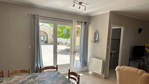 Habitación con mesa de comedor, sillas, sofá, radiador, televisor y vista al exterior.