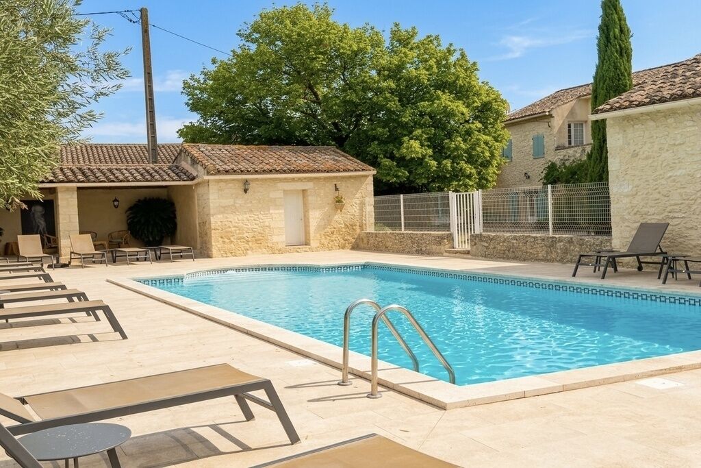 A swimming pool with lounge chairs and a small building, surrounded by trees and a stone wall.