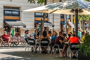 An outdoor seating area with tables and chairs, some with 'CIUDAD COMTAL' branding, under umbrellas.