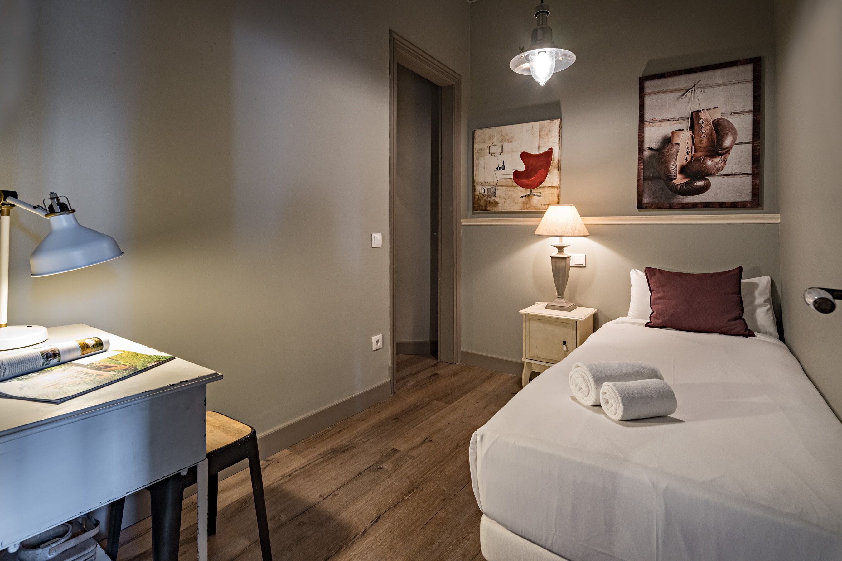 Una habitación de hotel con cama, escritorio con lámpara, silla y cuadros en la pared.