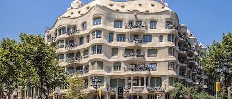 A multi-story building with unique architectural design, featuring balconies with sculptures, under a clear blue sky.