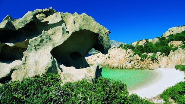Un paysage côtier caractérisé par une grande formation rocheuse, des eaux turquoise limpides et une plage de sable.