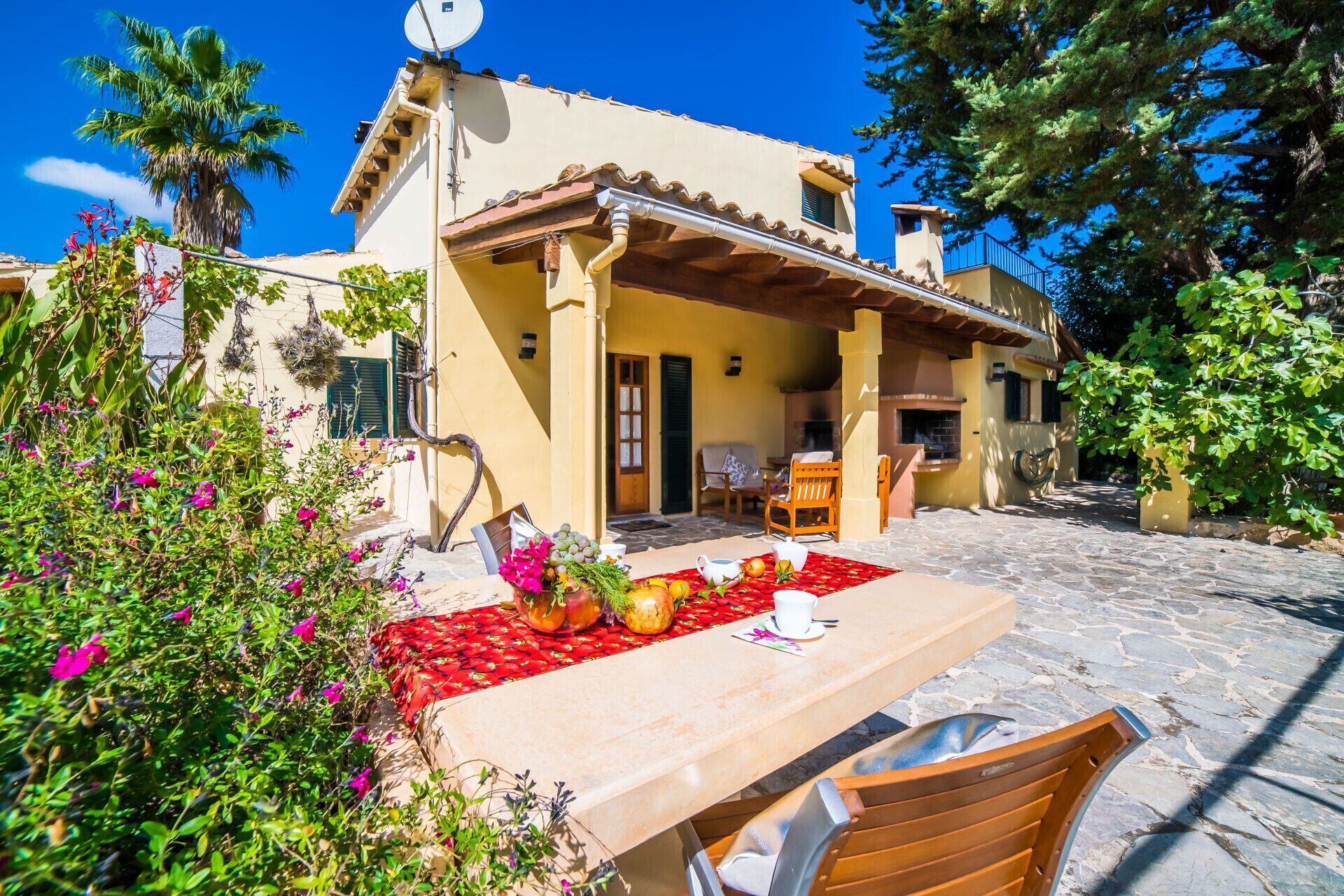 A Mediterranean-style villa with a stone patio, outdoor seating, and lush greenery.