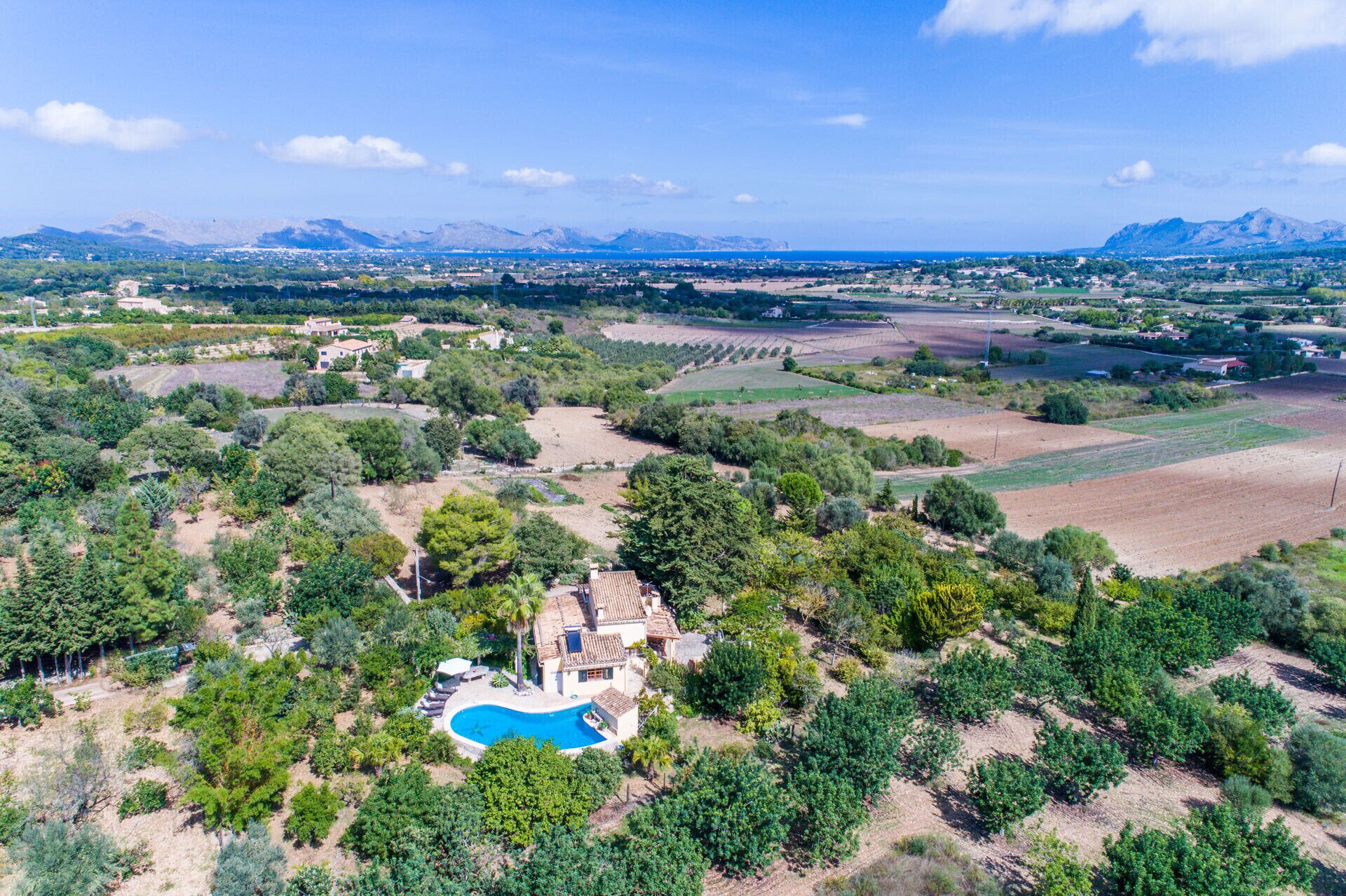 Une villa avec piscine, entourée d’arbres et de champs, avec des montagnes en toile de fond.