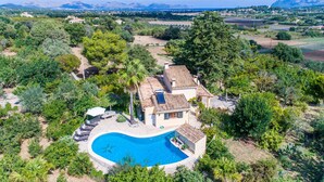 Een villa in mediterrane stijl met een zwembad, omgeven door weelderige begroeiing en bergen op de achtergrond.