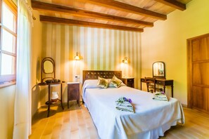 Une chambre d’hôtel comprenant un lit, deux tables de chevet, une petite table, une armoire en bois et une fenêtre avec des rideaux.