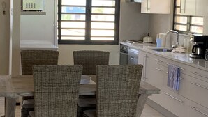A kitchen with a dining table, wicker chairs, a dishwasher, and a coffee maker. - Oceanfront Completely Upgraded Sand Dollar Resort  1 Bedroom Unit A2. Bari Reef (Bonaire)