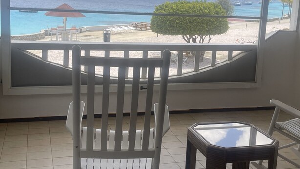 A balcony with a view of a beach, a small table, and a chair. - Oceanfront Completely Upgraded Sand Dollar Resort  1 Bedroom Unit A2. Bari Reef (Bonaire)