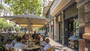 An outdoor café with yellow chairs and a large umbrella, surrounded by buildings and trees.