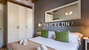 A neatly made bed with rolled towels, a large mirror above it, and the word "BARCELONA" on the wall.