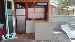 Een kleine keuken met een koelkast, spoelbak en een bord met een 'Ti-Punch Bar' er op.
