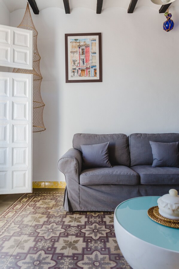 Un salón con un sofá gris, un tapete estampado, una obra de arte enmarcada y una puerta blanca.
