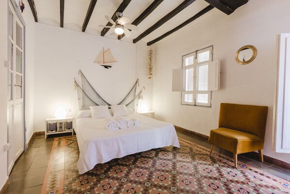Ein Schlafzimmer mit einem Bett, einem Sessel, einem Deckenventilator, einem Fenster und einem gestreiften Boden.