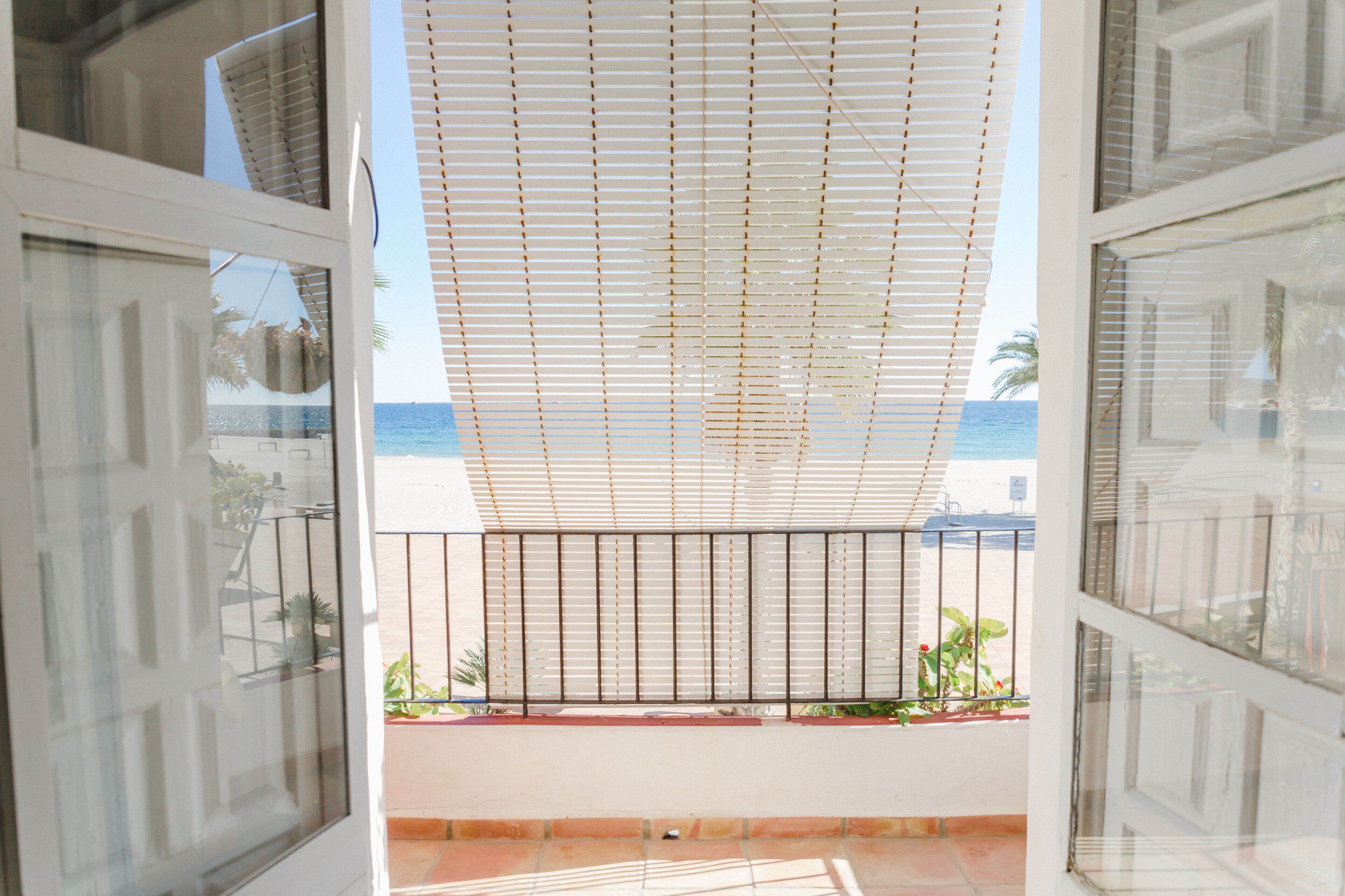 Een balkon met uitzicht op zee, een metalen hekwerk en bloempotten.