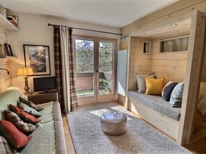 Quarto aconchegante com sofá, televisão, janela com cortinas e vista para uma montanha.