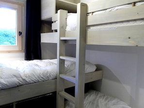 Huoneessa on kerrossänky, ikkuna, puinen tikapuu ja seinässä oleva kyltti.