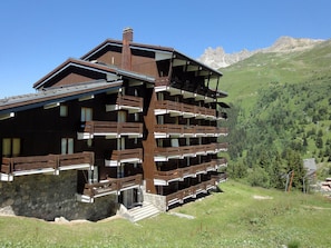 Een meerlaags houten chalet met balkons, met een bergachtig landschap op de achtergrond.