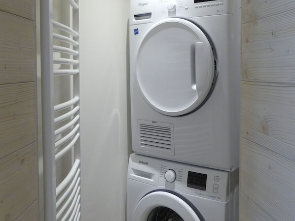 Een gestapelde wasmachine en droger in een wasserij, met een witte muur en een geventileerde droger.