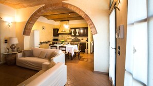 A cozy living room with a sofa, a dining table with chairs, and a kitchen in the background. - Apartment with pool and stunning landscape (Castelfiorentino)