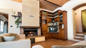 A spacious living area with a fireplace, wooden cabinets, and a cozy seating arrangement. - Apartment with pool and stunning landscape (Castelfiorentino)