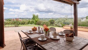 A covered outdoor dining area with a table set for breakfast, overlooking a scenic landscape. - Apartment with pool and stunning landscape (Castelfiorentino)