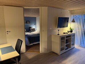Makuuhuoneessa on sänky, yöpöytä, työpöytä tuolilla, televisio ja ikkuna, jossa on sälekaihtimet.