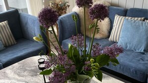 A living room with a sofa, a coffee table with a vase of flowers, and a framed picture on the table. - Beautiful holidayhouse with seaview and wellness area (Broager)