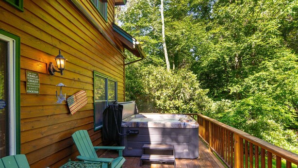 Une terrasse en bois avec un jacuzzi, deux fauteuils Adirondack et une rambarde en bois.