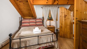 Une chambre avec un plafond en bois, un lit avec un oreiller à carreaux, une table de chevet avec une lampe et une armoire en bois.
