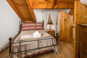 Ein Schlafzimmer mit Holzboden, einem Bett mit Kissenmuster, einem Nachttisch mit Lampe und einem Holzschrank.