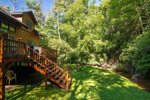 Eine Holzhütte mit einer Treppe zu einer Terrasse, umgeben von üppigem Grün und einem kleinen Bach.