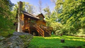 Une cabane en bois avec un escalier menant à une terrasse, le tout entouré d’une végétation luxuriante.