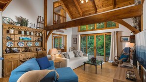 Un salon spacieux avec un plafond en bois, un canapé blanc, un divan bleu et un meuble en bois orné d’assiettes décoratives.