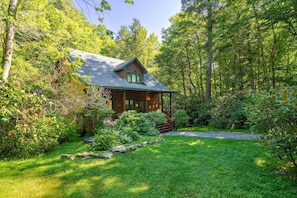 A rustic cabin with a sloped roof, surrounded by lush greenery and a well-maintained garden. - Boone Cabin with Private Waterfall, Hot Tub & Fire Pit (Boone)