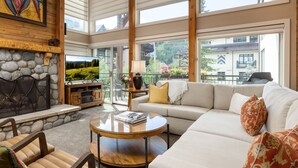 Ein geräumiges Wohnzimmer mit Kamin aus Stein, einem großen Fernseher, einer Couch und einem Balkon mit Blick auf die Umgebung.