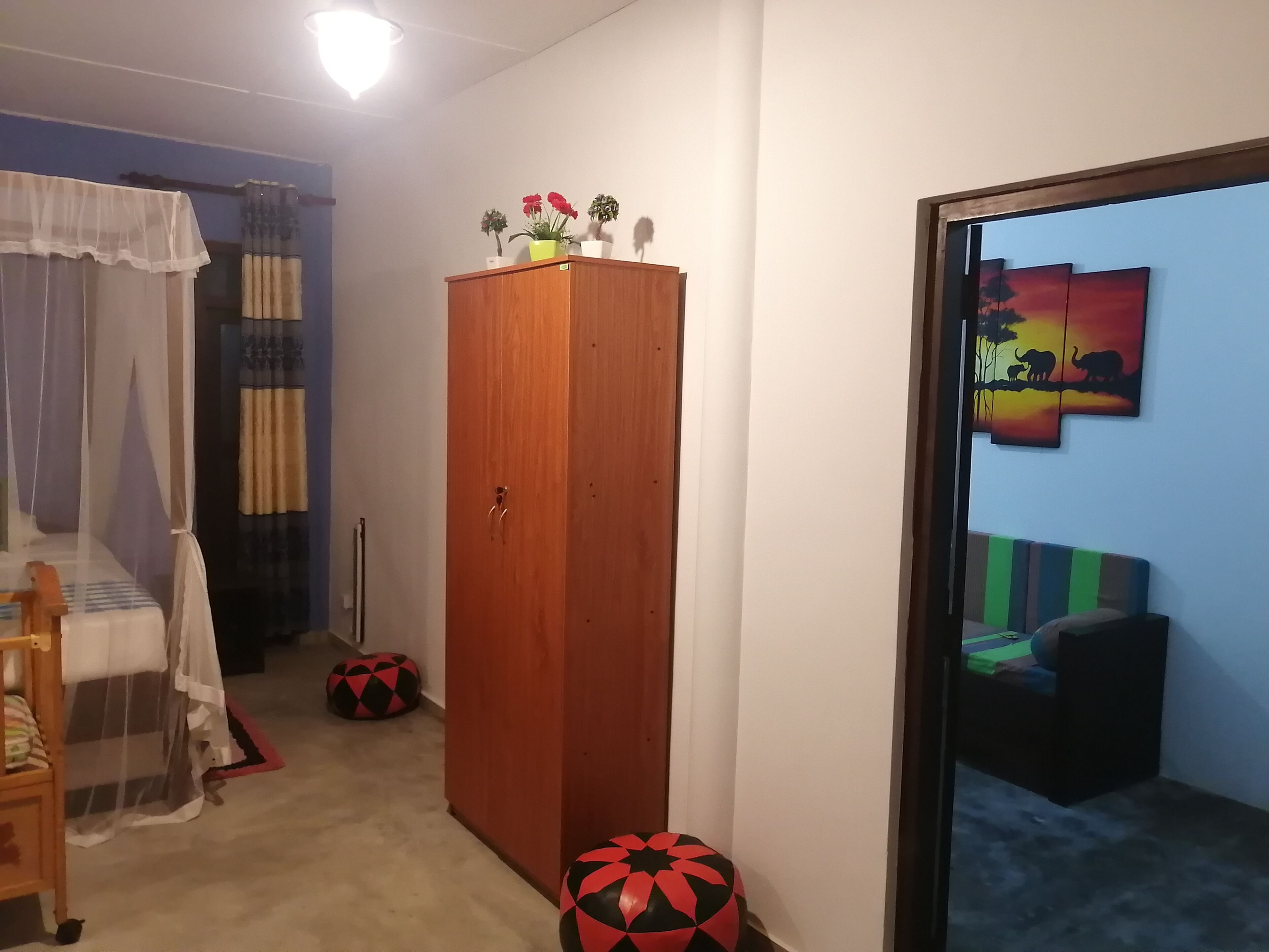 Ein Schlafzimmer mit Bett, Kleiderschrank, Nachttisch, Lampe und einem Fenster mit Blick nach draußen.