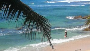 A beach with clear blue water, a person in the water, and palm trees. - Happy Beach (Unawatuna)