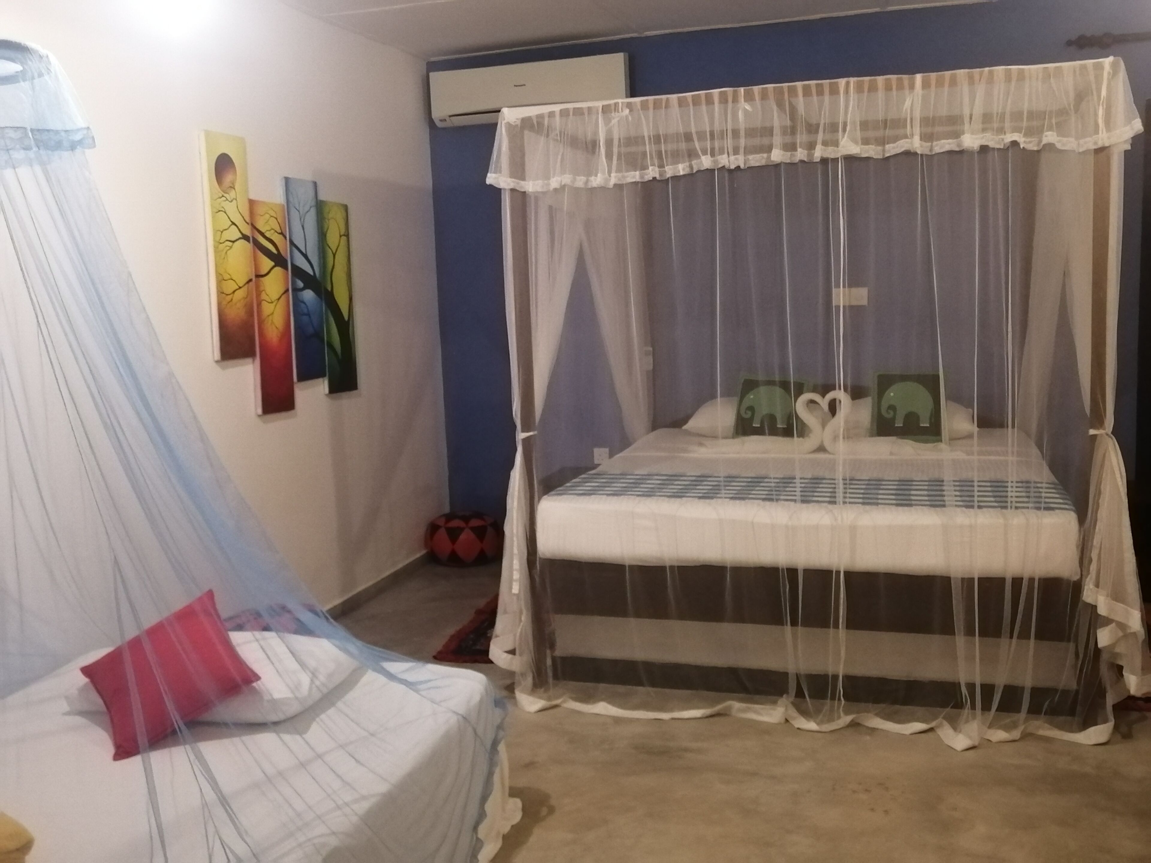 A bedroom with a bed covered by a mosquito net, a bedside table, and a wall-mounted air conditioner.