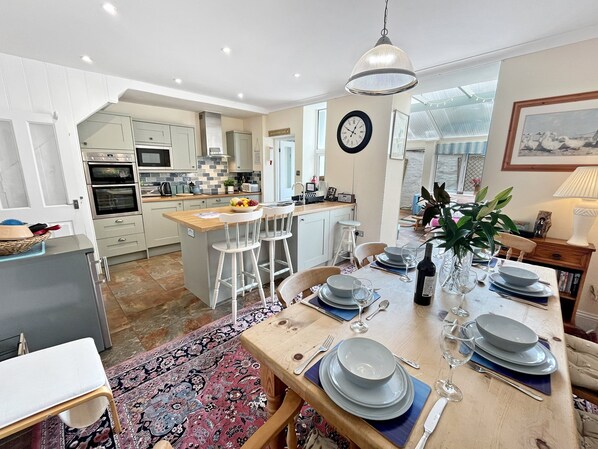A modern kitchen with white cabinets, a central island with stools, and a dining area set for six with plates, glasses, and cutlery.