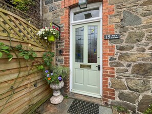 A stone building with a green door, a wooden fence, and a hanging flower pot. - Pip's Corner, Lynton (Lynton)